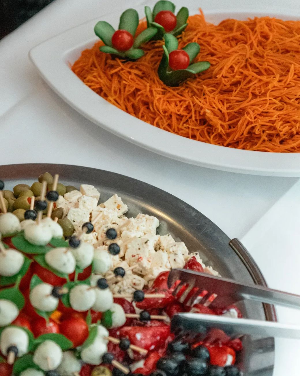 Antipasti-Platte mit Mozzarella-Spießen, Feta und Oliven, dahinter Karottensalat