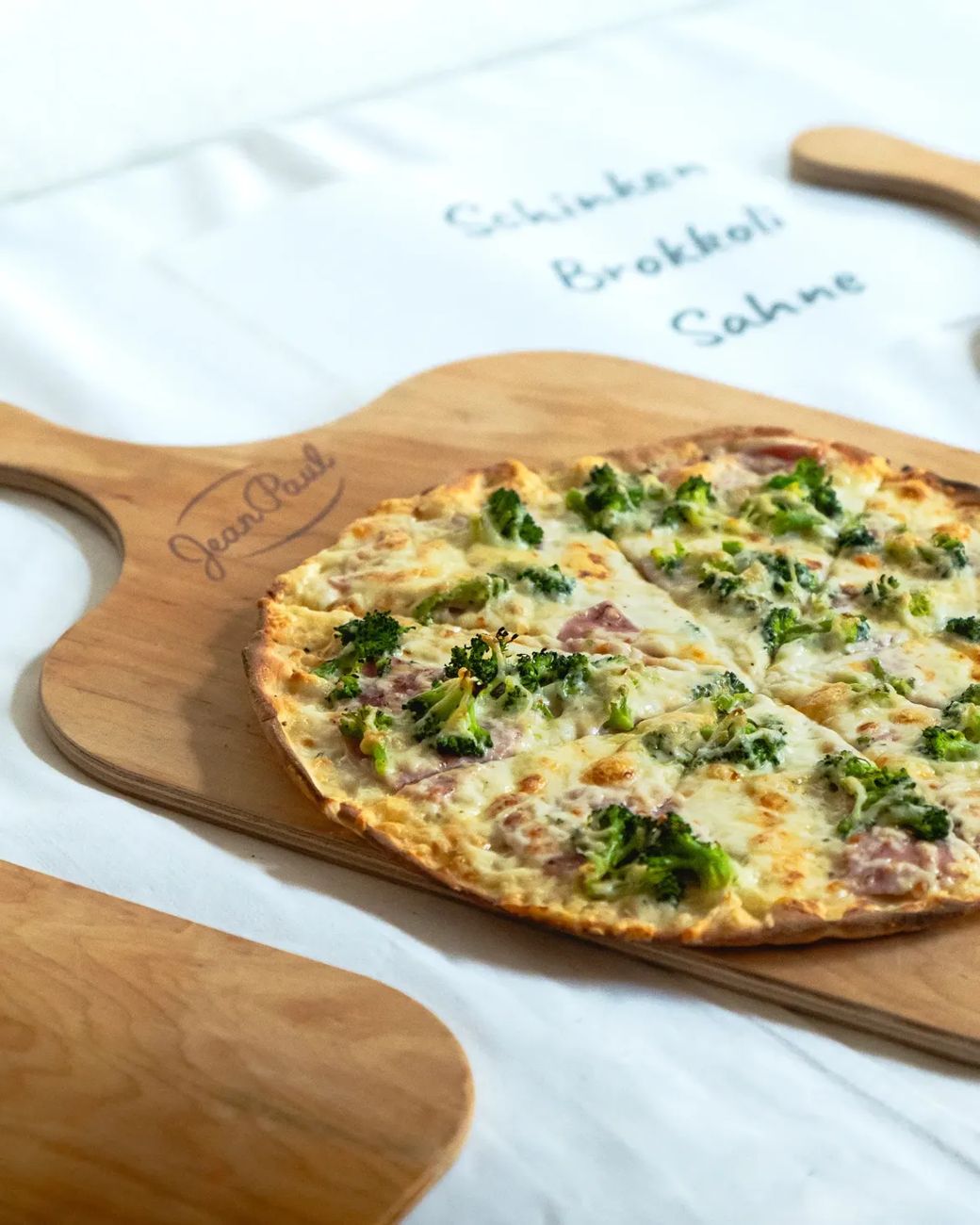Pizza Schinken, Brokkoli, Sahne auf einem Holzbrett