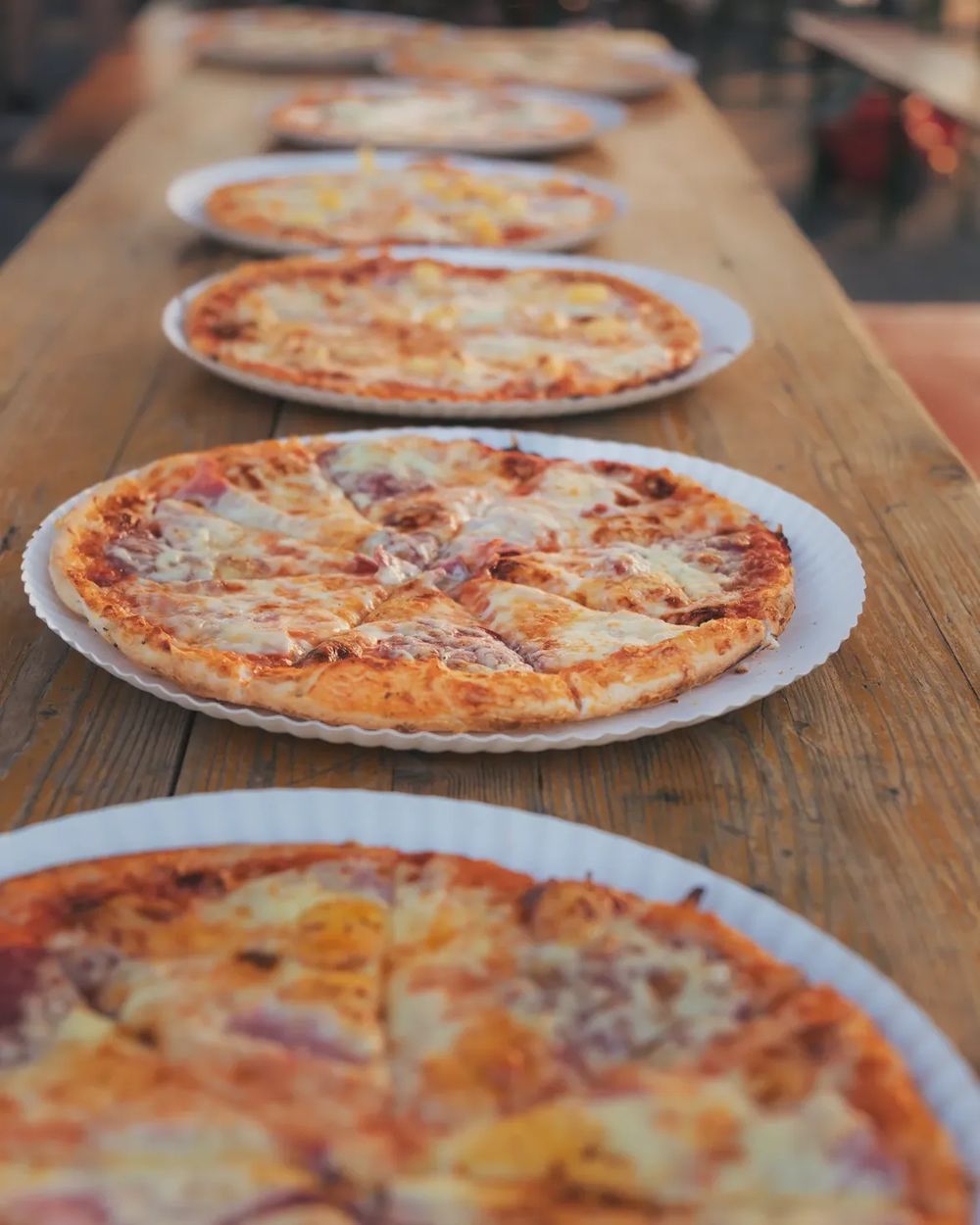 Eine Reihe geschnittener Pizzen auf einem langen Holztisch